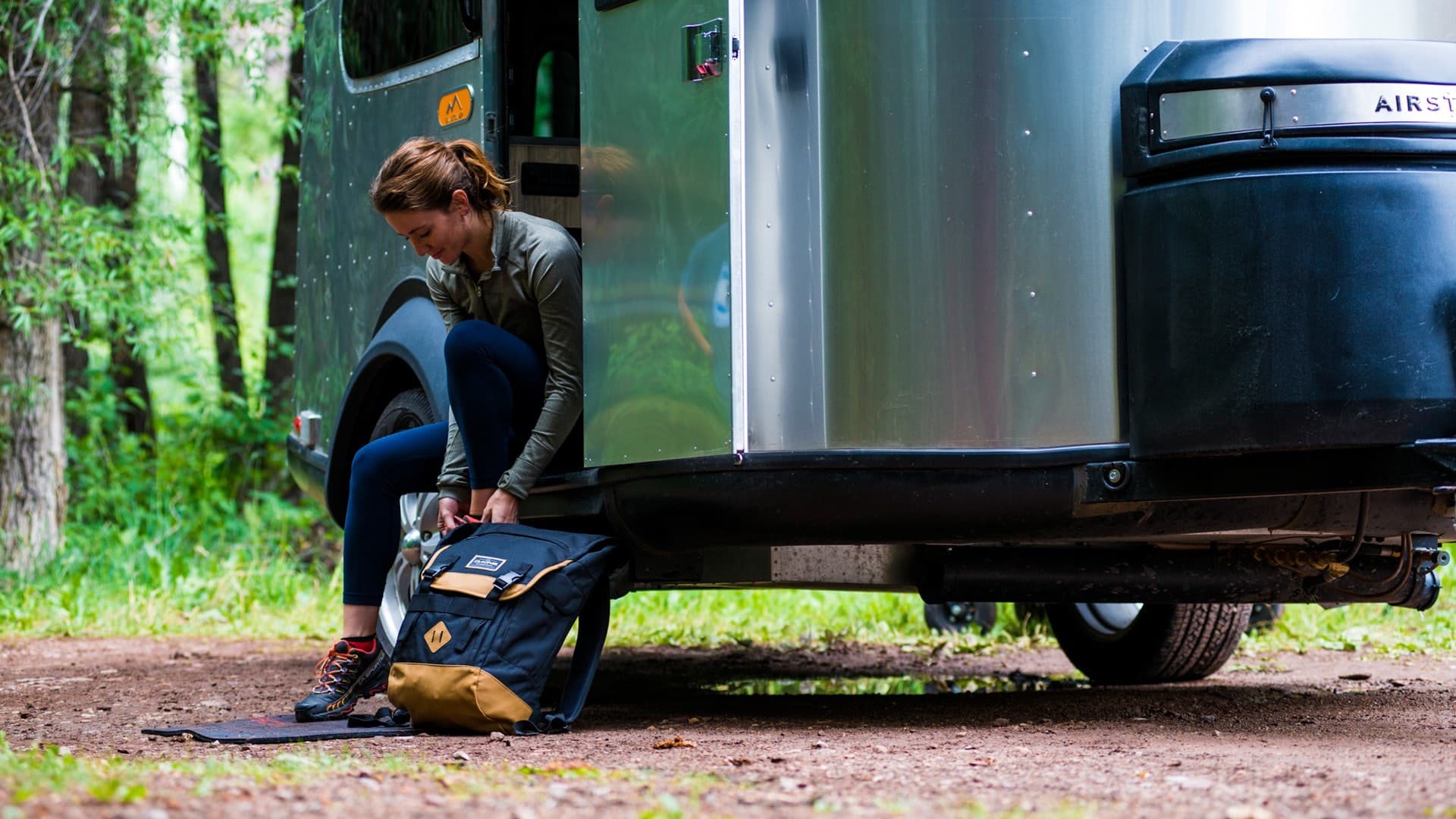 Woman packing backpack at Airstream trailer door with outdoor scenery