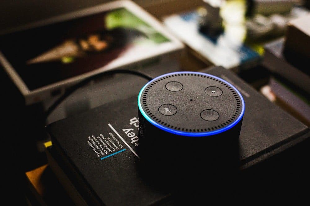 Amazon Alexa smart speaker with blue glowing ring on desk with magazines