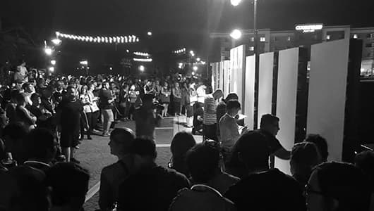 Black and white photograph of crowded outdoor nighttime street festival or market