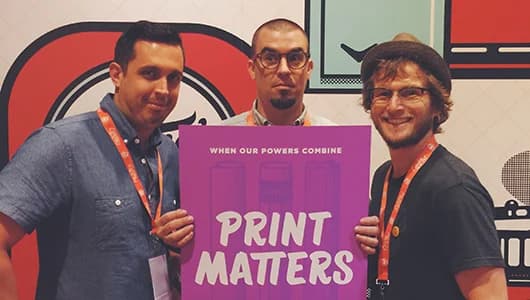 Three people holding purple sign reading When Our Powers Combine Print Matters