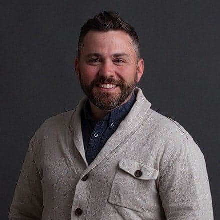 Headshot of a smiling man in casual button-up shirt against gray background