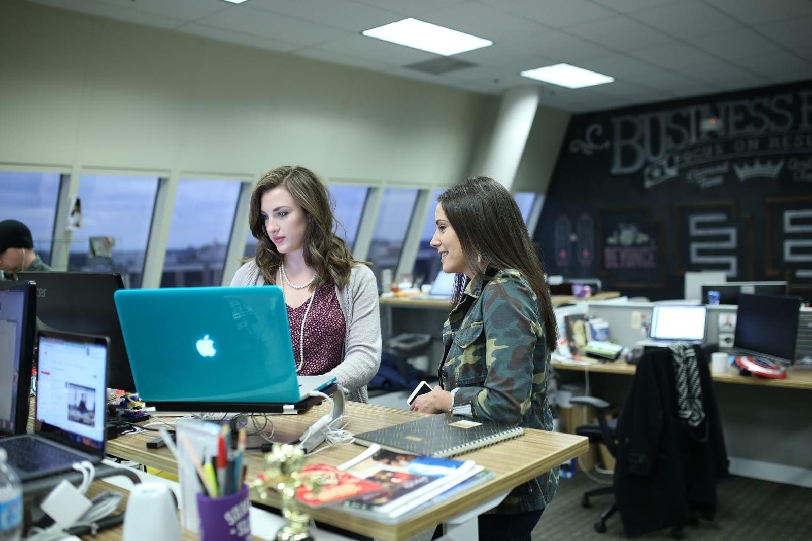 Two women collaborating on laptop at modern office desk