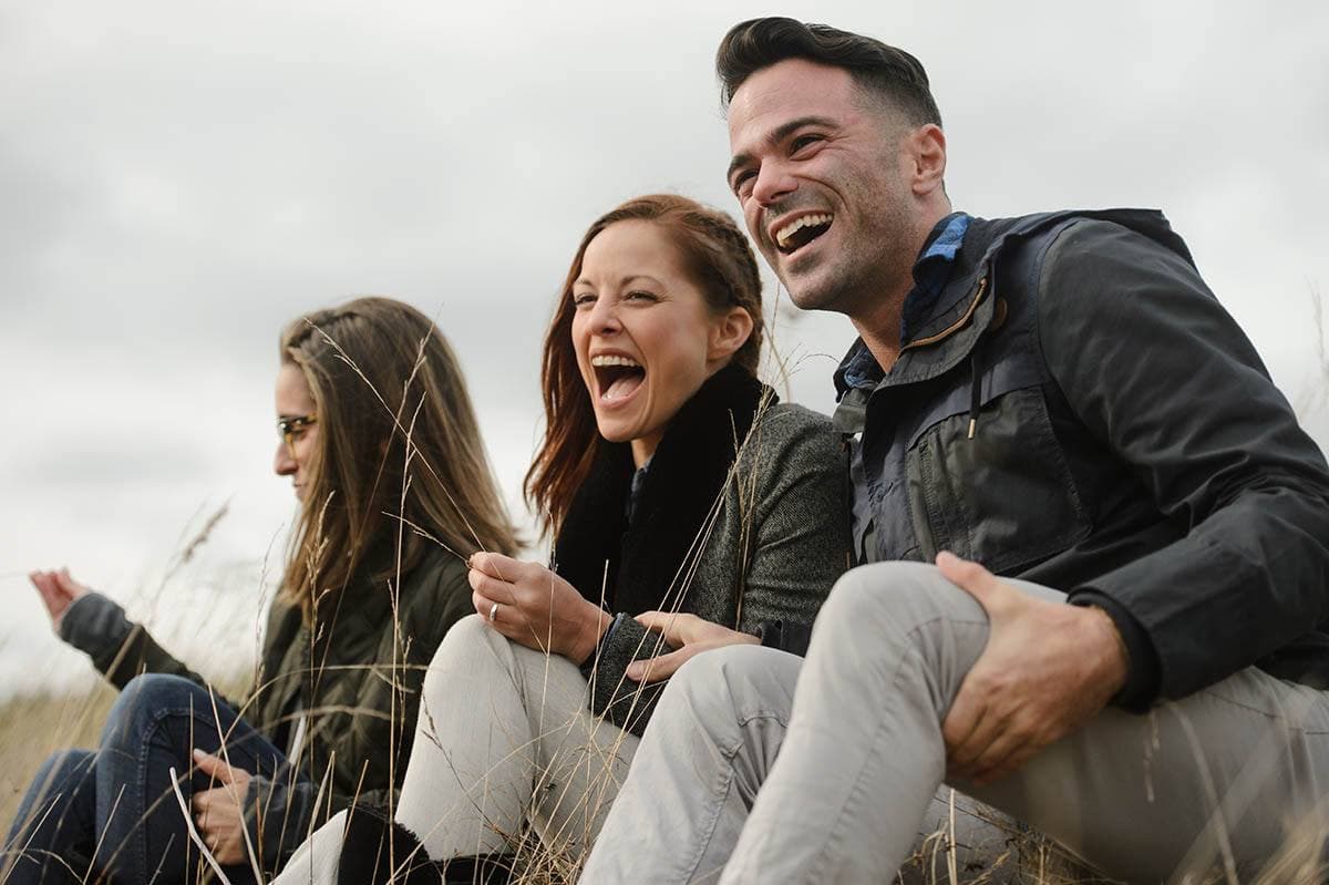 Four people laughing together in autumn field setting with natural lighting