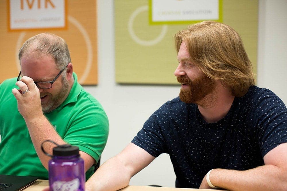 Two men at meeting table with microphone, one in green shirt