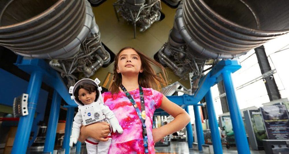 Child holding American Girl doll in front of rocket engines