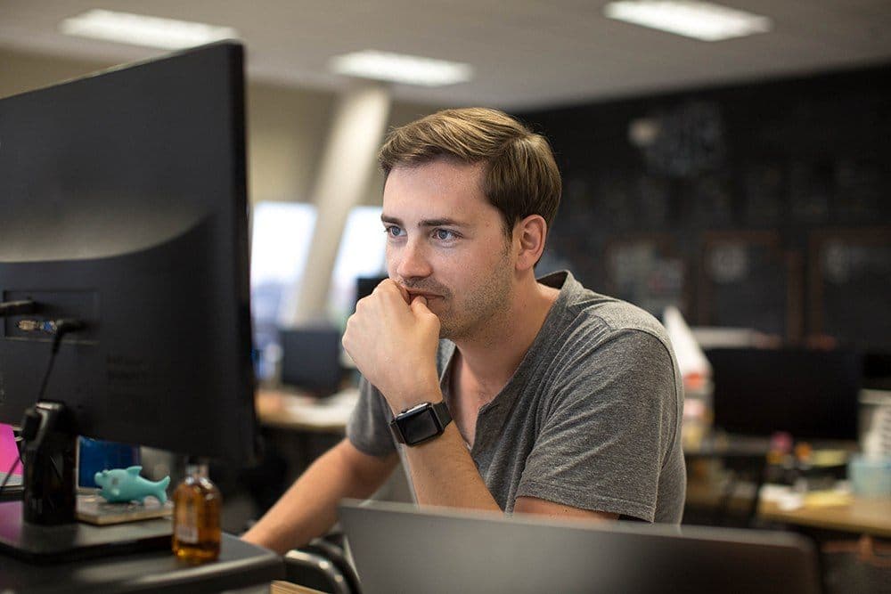 Headshot of man in gray shirt at desk with computer