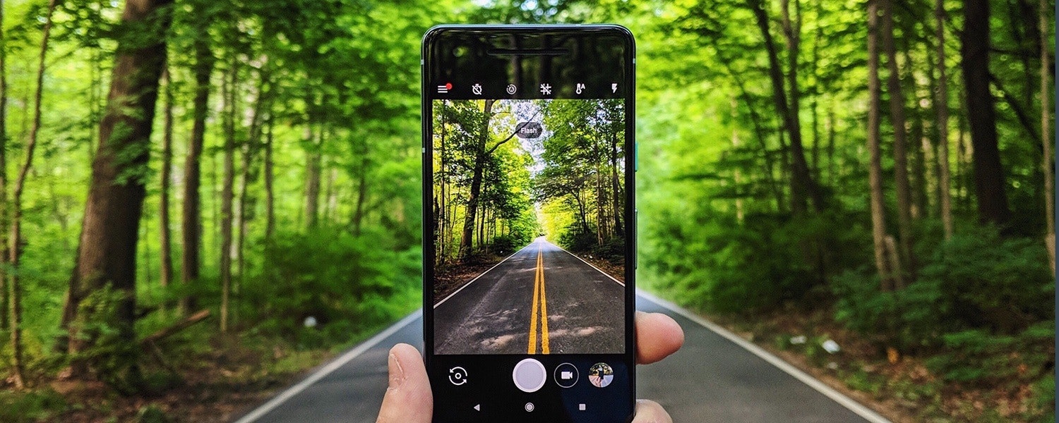 Individual taking a photo of a road through a wood on their smartphone