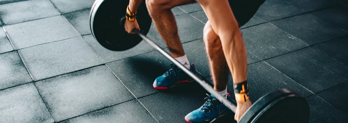 close up of a man's legs as he lifts a barbell off the ground