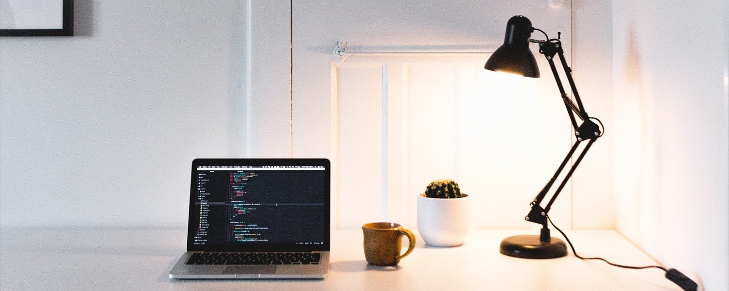 a desk lamp illuminating a laptop, a coffee mug and a succulent