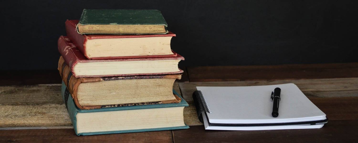 stack of books, a notebook and pen on a desk