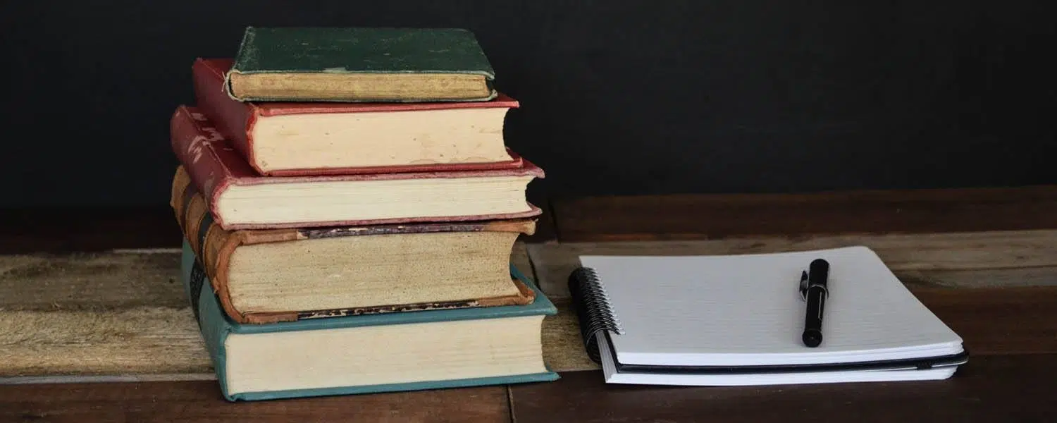 stack of books, a notebook and pen on a desk