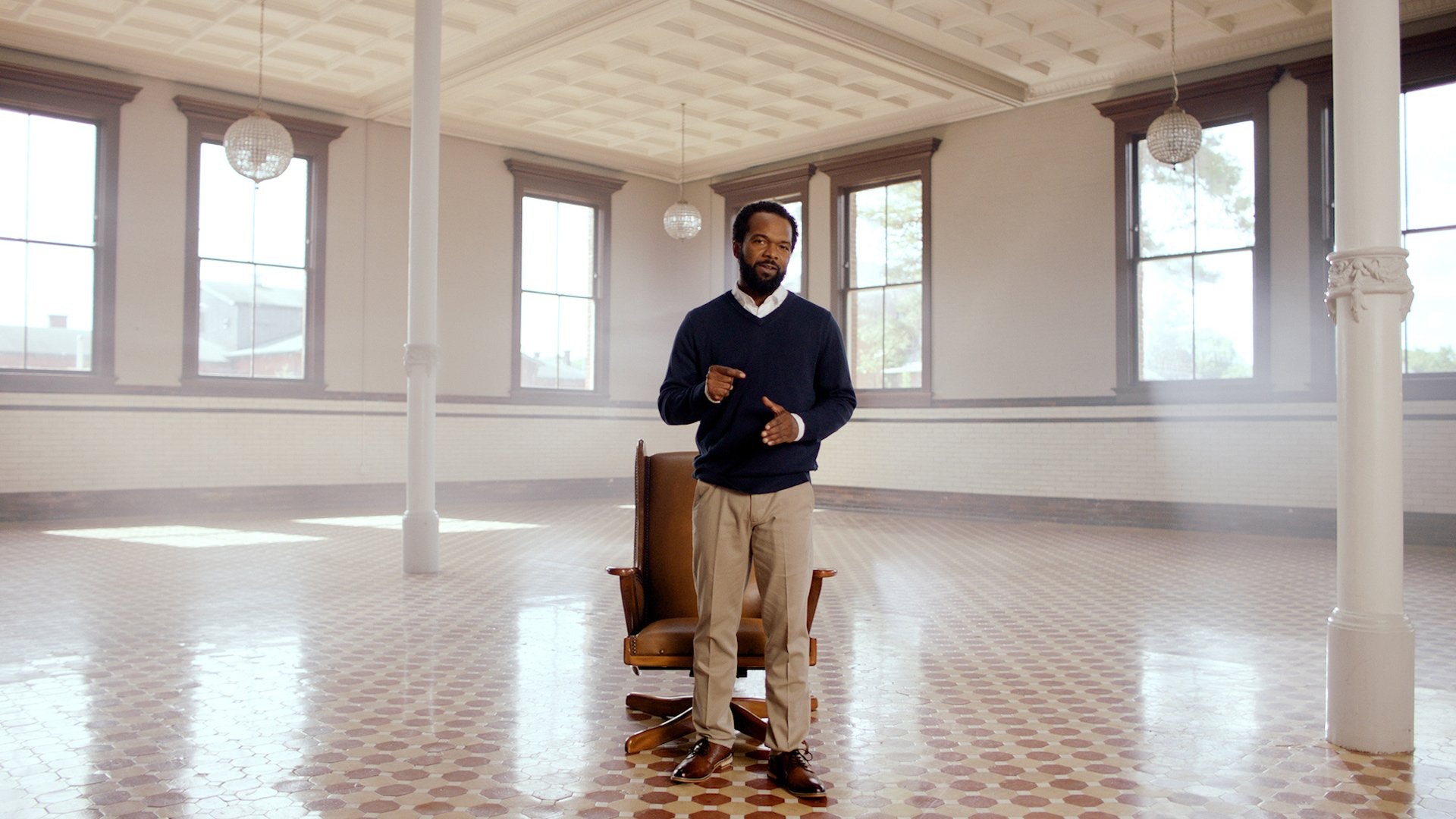 man standing up from chair and talking in large room