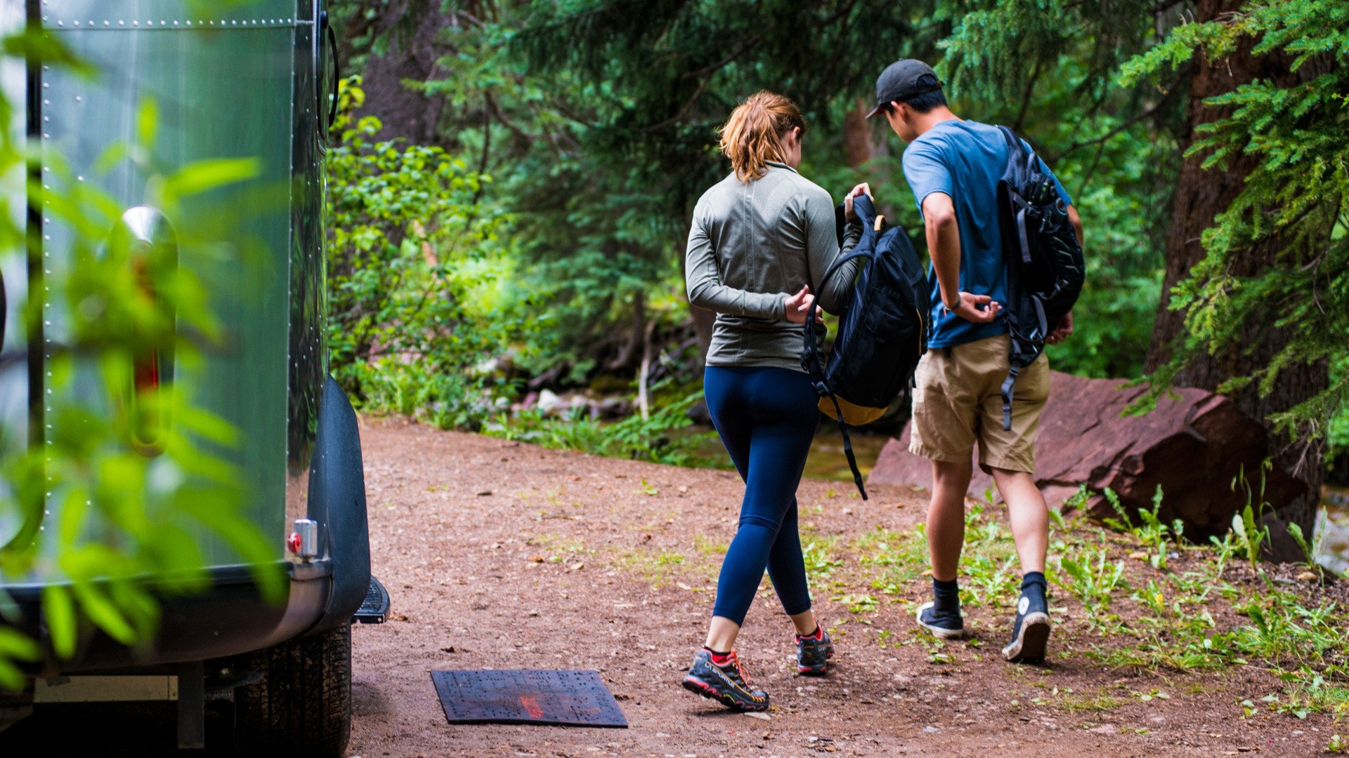 A Woman and Man Walking Out of Basecamp Travel Trailer into Forest