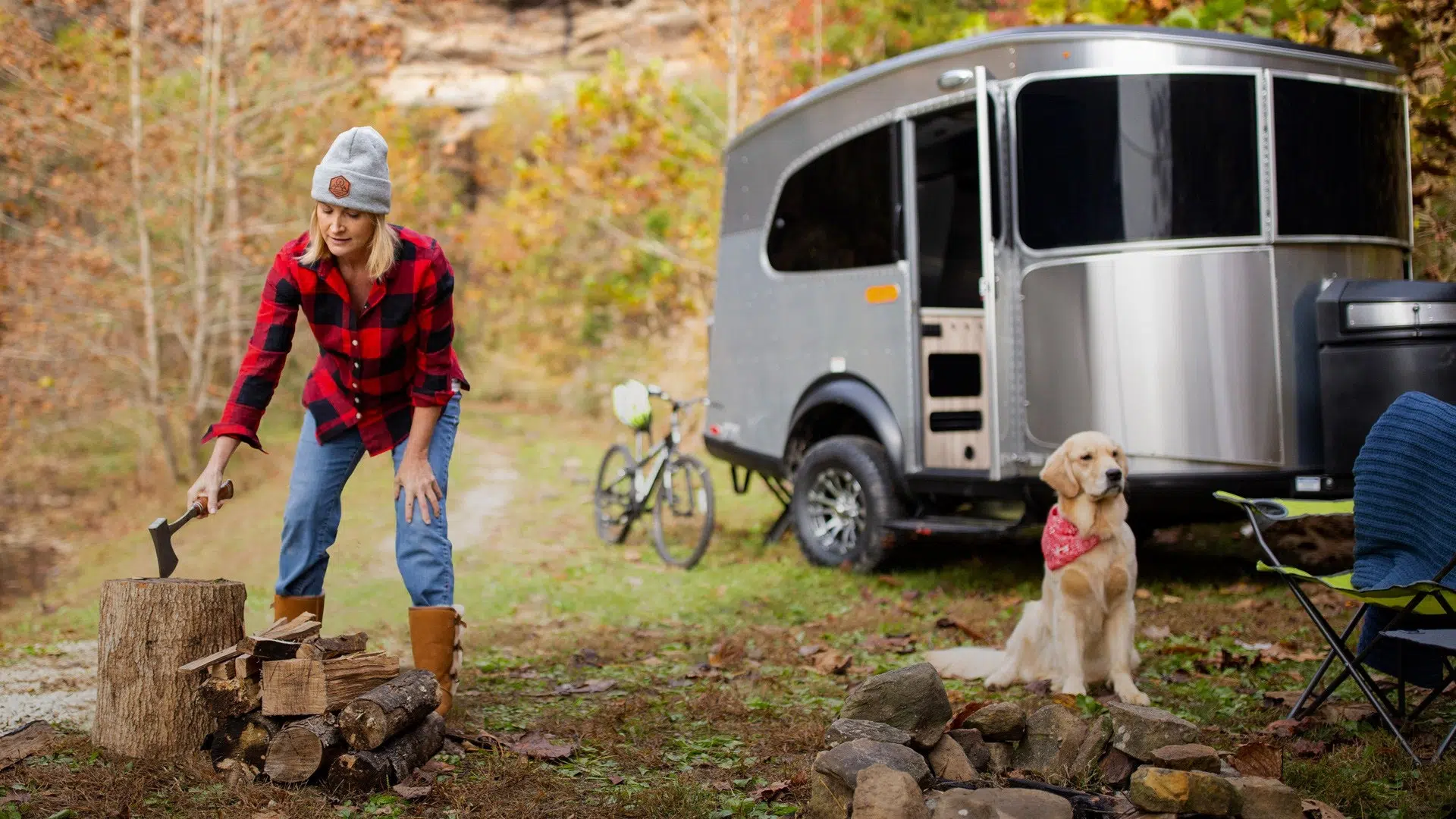 Woman and Dog Chopping Wood in Front of Airstream Basecamp